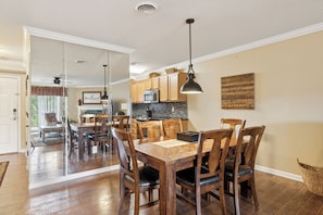 A dining area with a wooden table and chairs, a kitchen in the background, and a view into another room. - 2 BR | Indoor Pool | Hot Tub Access | Mtn View (Pigeon Forge)