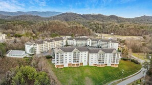 A multi-story hotel with a central courtyard, surrounded by a forested landscape and mountains in the background.