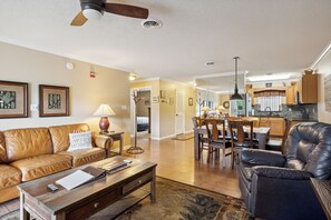 A living room with a leather sofa, a coffee table, and a dining area with a wooden table and chairs.