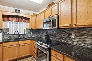 A kitchen with wooden cabinets, a stainless steel microwave, a stove, and a tiled backsplash.