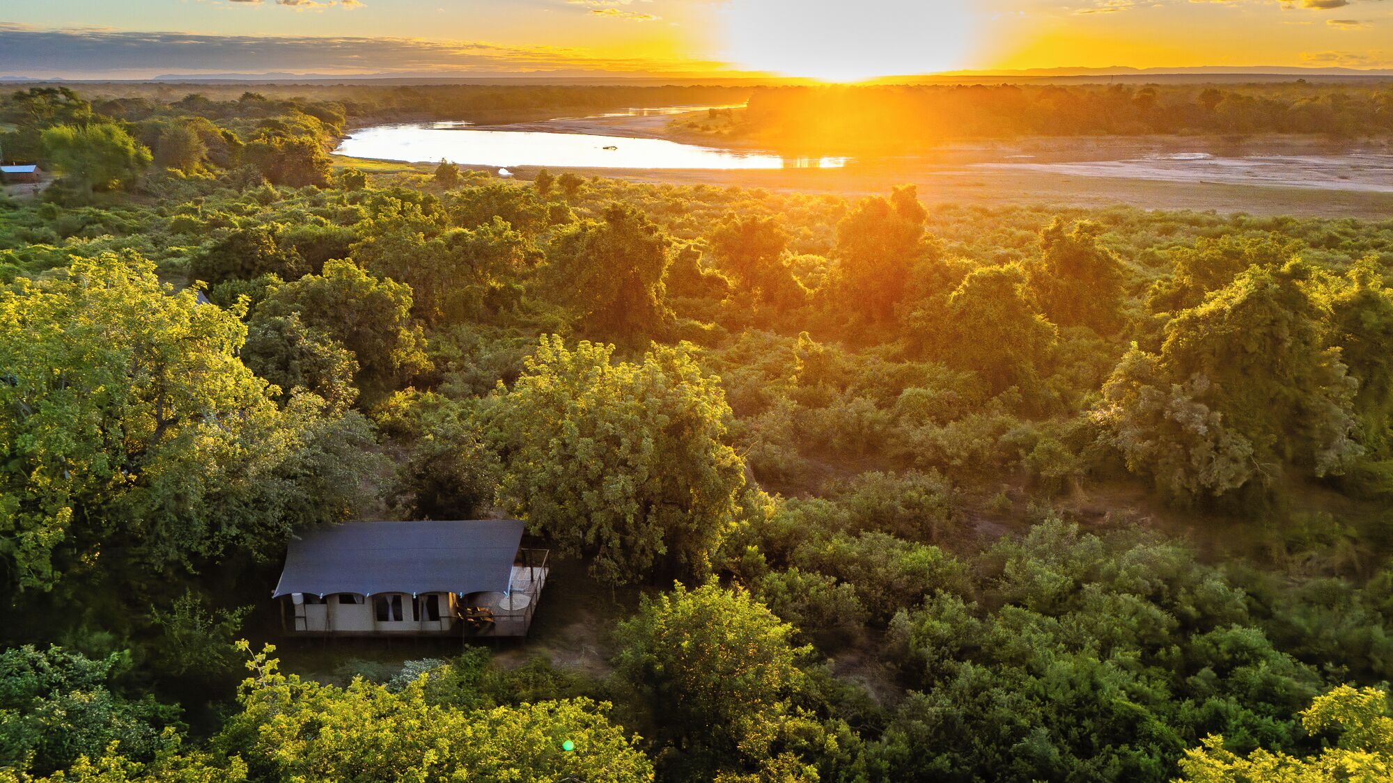 Una casa rodeada de abundante vegetación con un río al fondo.