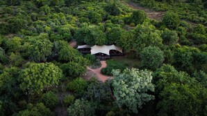 An aerial view of a secluded eco-lodge surrounded by dense forest, featuring a central structure with a thatched roof and wooden deck. - Camp Sabali & Safaris (South Luangwa National Park)