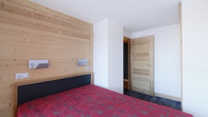 Une chambre à coucher avec une tête de lit en bois, une couvre-lit rouge et une porte donnant sur une autre pièce.