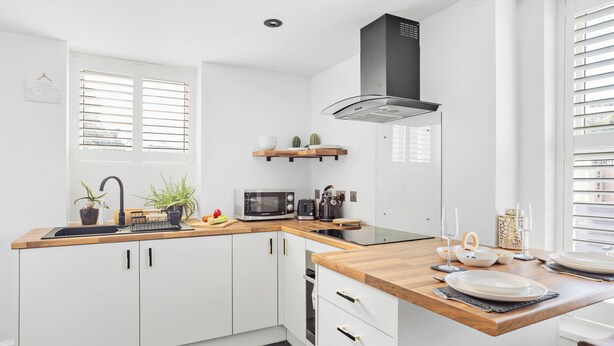 A modern kitchen with white cabinets, a wooden countertop, a microwave, and a black range hood. - Peaceful, Homely, Pet Friendly with Free Parking - Holiday Apartment 13A (Torquay)