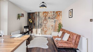 A modern living room with a wooden dining table, a leather sofa, a white rug, and a unique patterned wall. - Peaceful, Homely, Pet Friendly with Free Parking - Holiday Apartment 13A (Torquay)