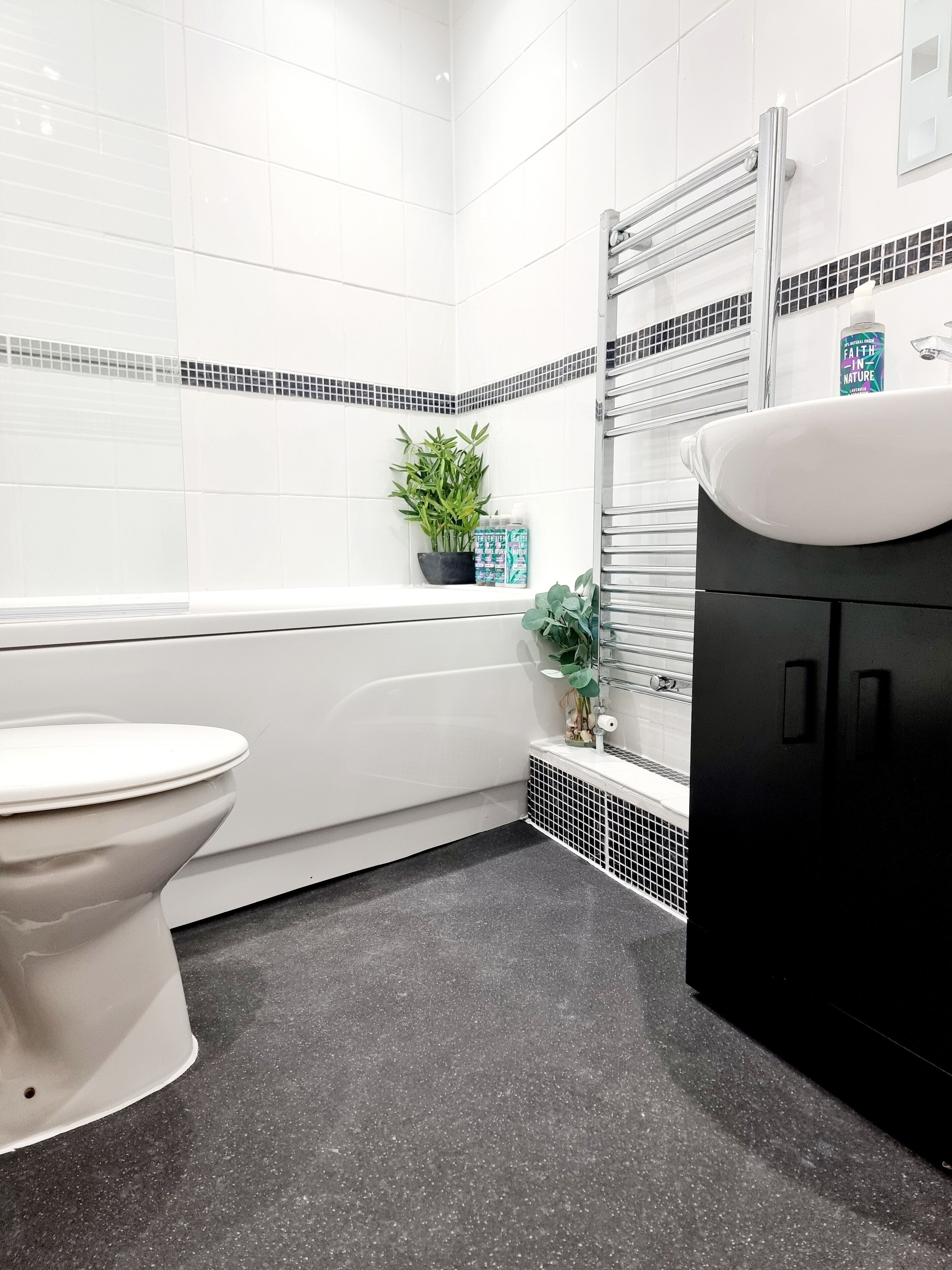 A modern bathroom with a white toilet, a bathtub, and a black vanity.