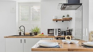 A modern kitchen with white cabinets, a wooden countertop, and a black range hood. There are two stools and a dining table set with plates and glasses. - Peaceful, Homely, Pet Friendly with Free Parking - Holiday Apartment 13A (Torquay)