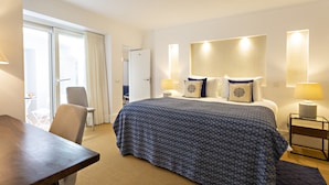 A hotel room with a bed, a desk, a chair, a lamp, and a window with curtains. - Townhouse in Tavira With 2 Bedrooms and 2 Bathrooms (Tavira)