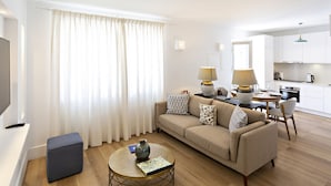 A modern living room with a sofa, coffee table, and lamps. There is a kitchen area with cabinets and a dining table. - Townhouse in Tavira With 2 Bedrooms and 2 Bathrooms (Tavira)