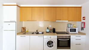 Una cocina compacta con electrodomésticos blancos, armarios de madera y una lavadora.