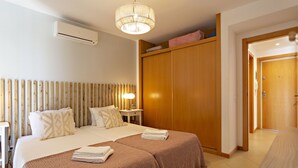 Una habitación de hotel con una cama grande, un armario de madera, una mesita de noche con lámpara y un equipo de aire acondicionado.