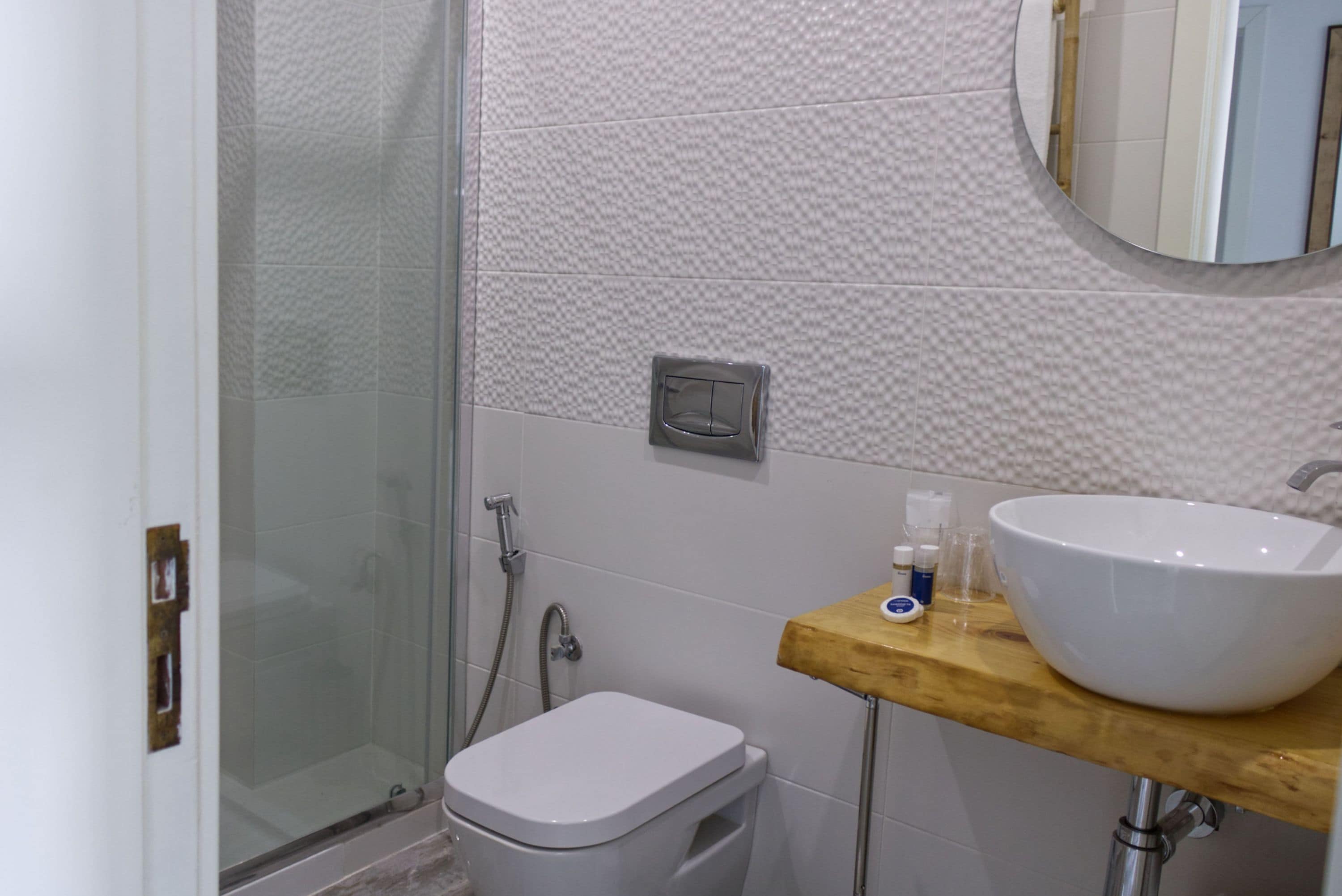 A bathroom with a glass shower enclosure, a toilet, a sink with a wooden countertop, and a mirror above the sink.