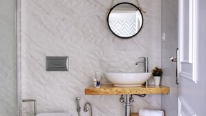 Un baño con inodoro blanco, estante de madera con lavabo sobre encimera, espejo y ducha.