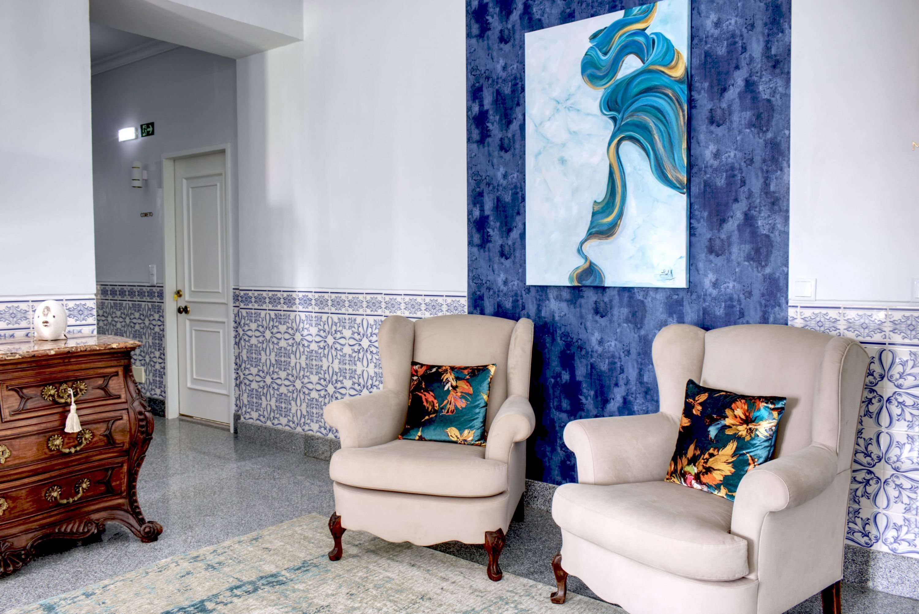 Een hal met twee fauteuils, een houten dressoir en een blauw-witte wandbekleding.