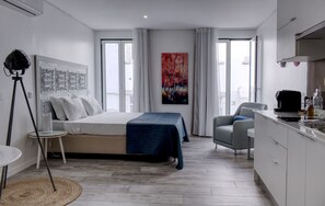 Ein modernes Schlafzimmer mit einem Bett, einem Schreibtisch und einem Stuhl. An der Wand hängt ein Gemälde und ein Fenster mit Vorhängen.