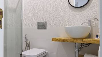 A bathroom with a white toilet, a wooden vanity, a white sink, and a mirror.