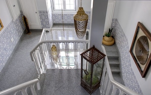 Una scala con un parapetto in vetro, ringhiere bianche e lampade decorative pendenti.