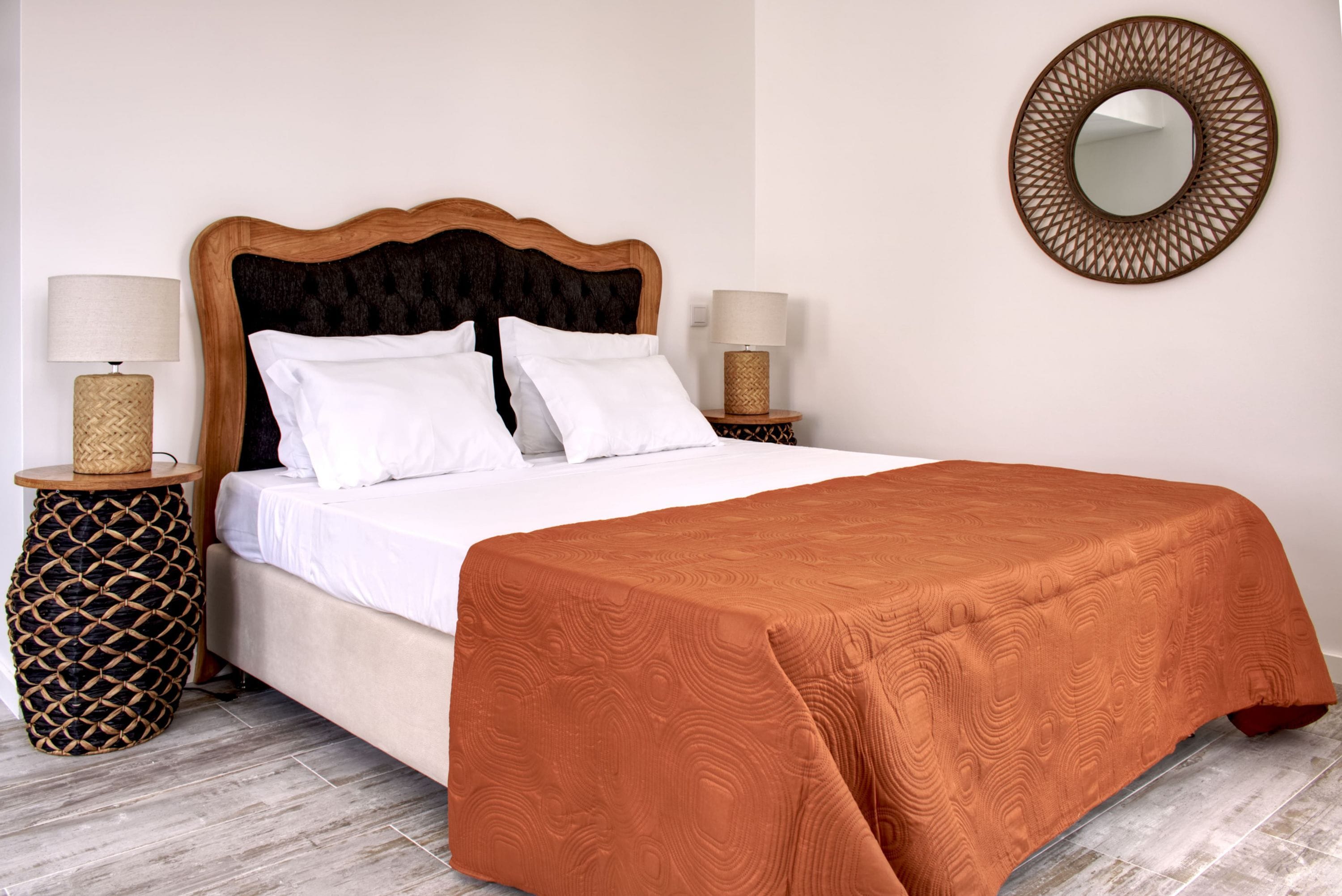 A neatly made bed with a wooden headboard, two bedside tables with lamps, and a round mirror on the wall.