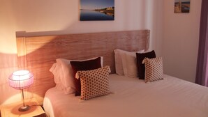 Una cama bien hecha con un cabecero de madera, una lámpara de noche y dos cuadros colgados en la pared.