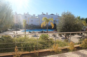 Uma área de piscina com espreguiçadeiras e guarda-sóis, cercada por vegetação e um edifício com várias janelas e varandas.