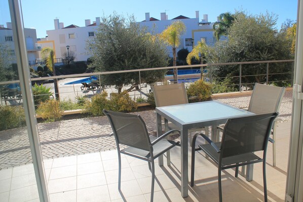 A balcony with a table and chairs, overlooking a swimming pool and buildings.
