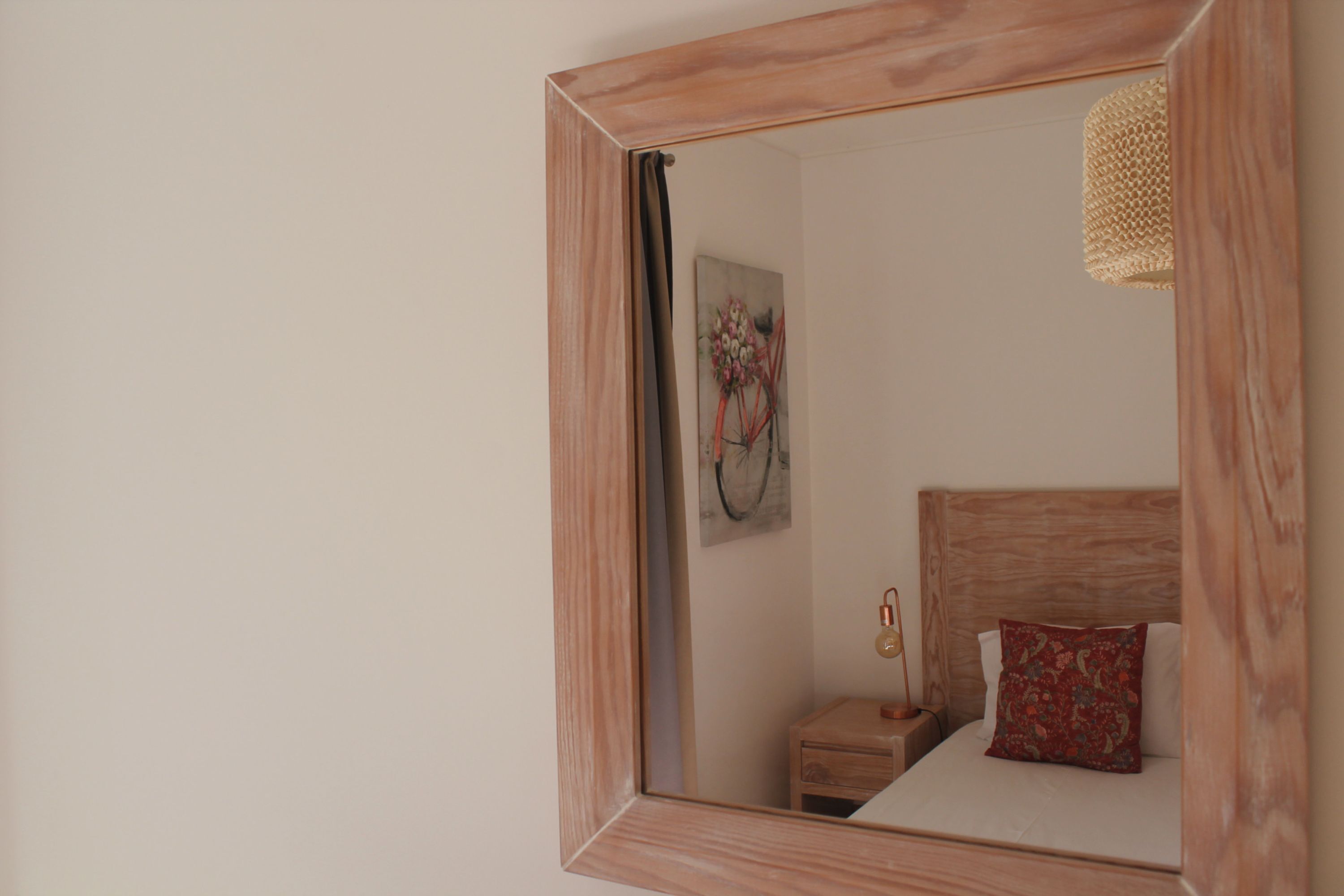 Une chambre à coucher avec un miroir à cadre en bois, une table de chevet avec une lampe et un lit avec un oreiller rouge.