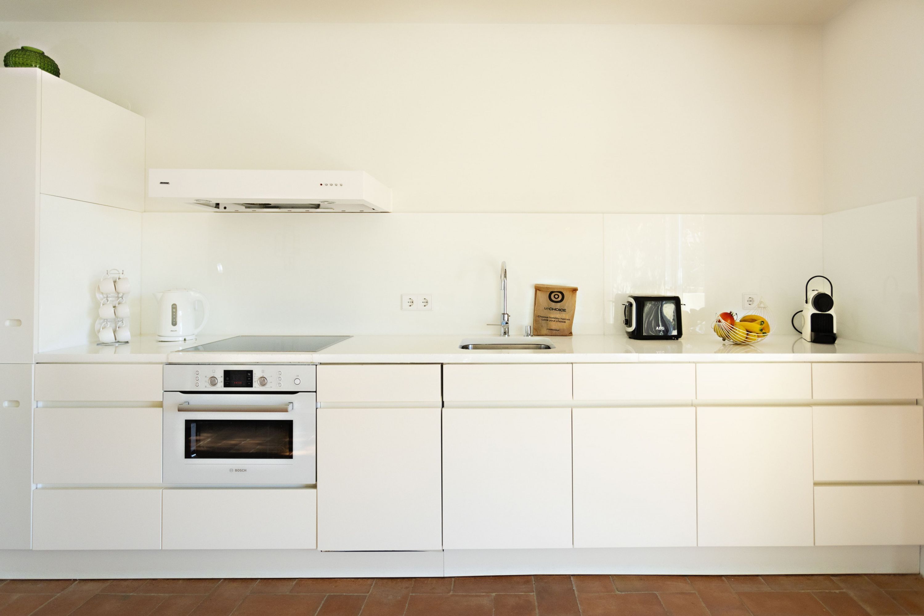 A modern kitchen with white cabinetry, a Bosch oven, a coffee maker, and a fruit basket.