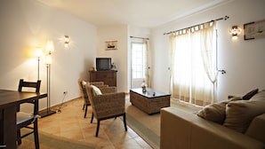 A living room with a sofa, chairs, a coffee table, a TV, and a window with curtains. - Cabanas Village in Tavira (Tavira)