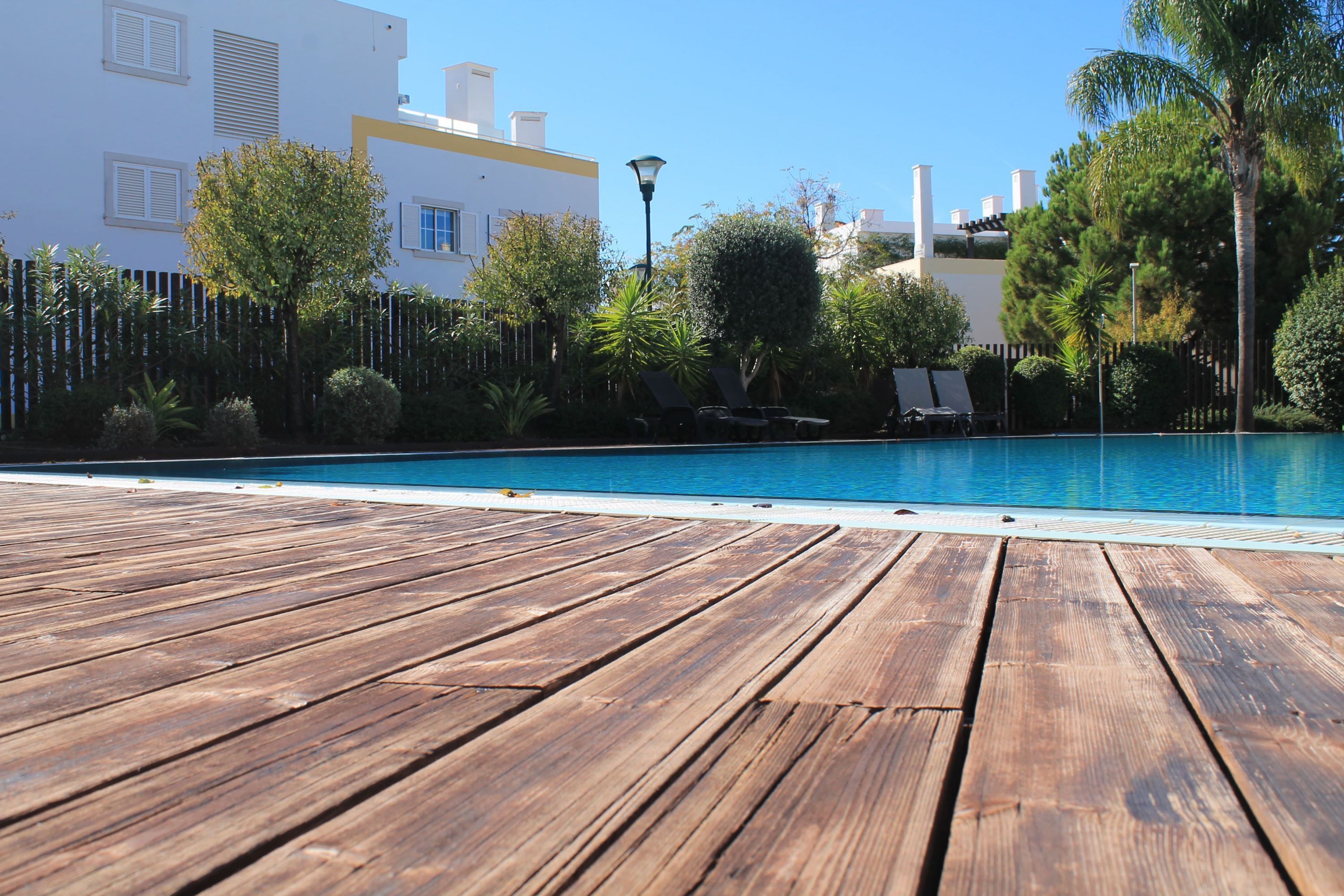 A wooden deck leading to a swimming pool with lounge chairs and a fence.