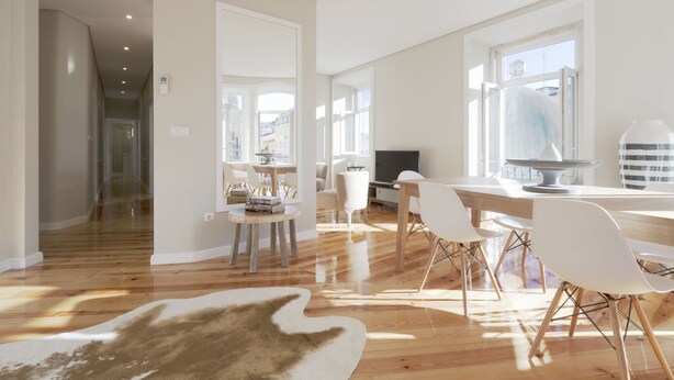 A spacious living room with a wooden floor, a large window, and a dining area with white chairs and a table. - Andrade in Lisboa Ciudad (Lisbon)