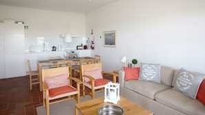 Une cuisine moderne avec des appareils électroménagers blancs, un coin repas avec des chaises et une table en bois, et un salon avec un canapé et des coussins décoratifs.