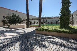 A courtyard with cobblestone paving, palm trees, and a pool area. - CV C - Salinas - Convento das Bernardas (Tavira)