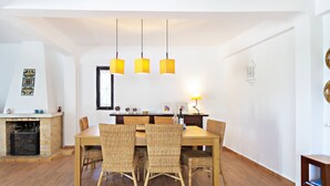 A dining area with a wooden table and wicker chairs, a fireplace, and hanging pendant lights. - Casa Z lia in Tavira (Tavira)