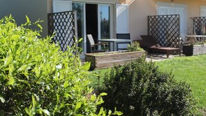 A modern outdoor seating area with a table and chairs, a wooden planter, and a small hedge. - CG 71M - Dplx Garden - Cabanas Gardens (Tavira)