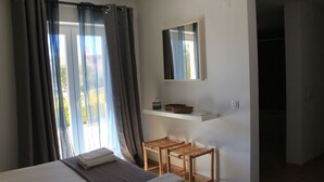 Un dormitorio con cama, una mesita, un espejo y una ventana con cortinas.