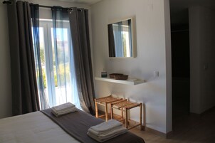 Um quarto com uma cama, uma mesinha, um espelho e uma janela com cortinas.