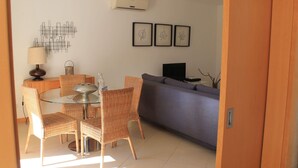 Un comedor con sillas de mimbre y una mesa de vidrio, un sofá gris y arte mural con hojas enmarcadas.