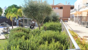 Balcón con baranda de metal que da a una zona de piscina con sillones y sombrillas.