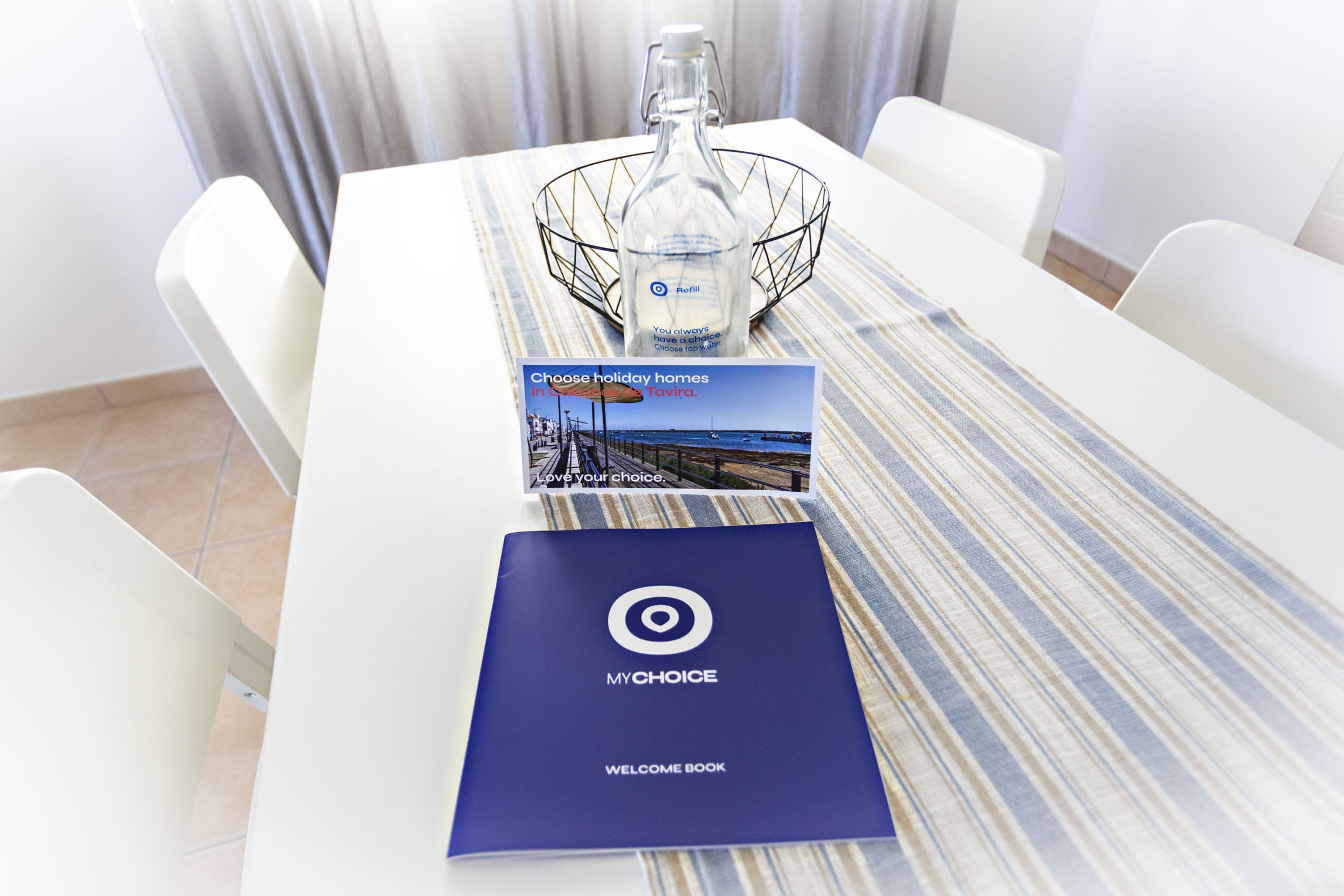 Ein Hotelzimmer mit gestreiftem Tischläufer, einem Begrüßungsbuch, einer Broschüre und einer Glasflasche.