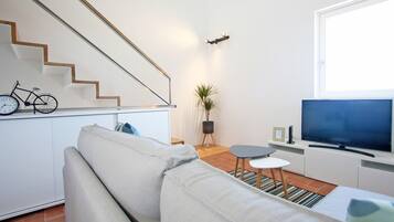 Una sala de estar moderna con un sofá, un televisor, una mesita y una escalera.