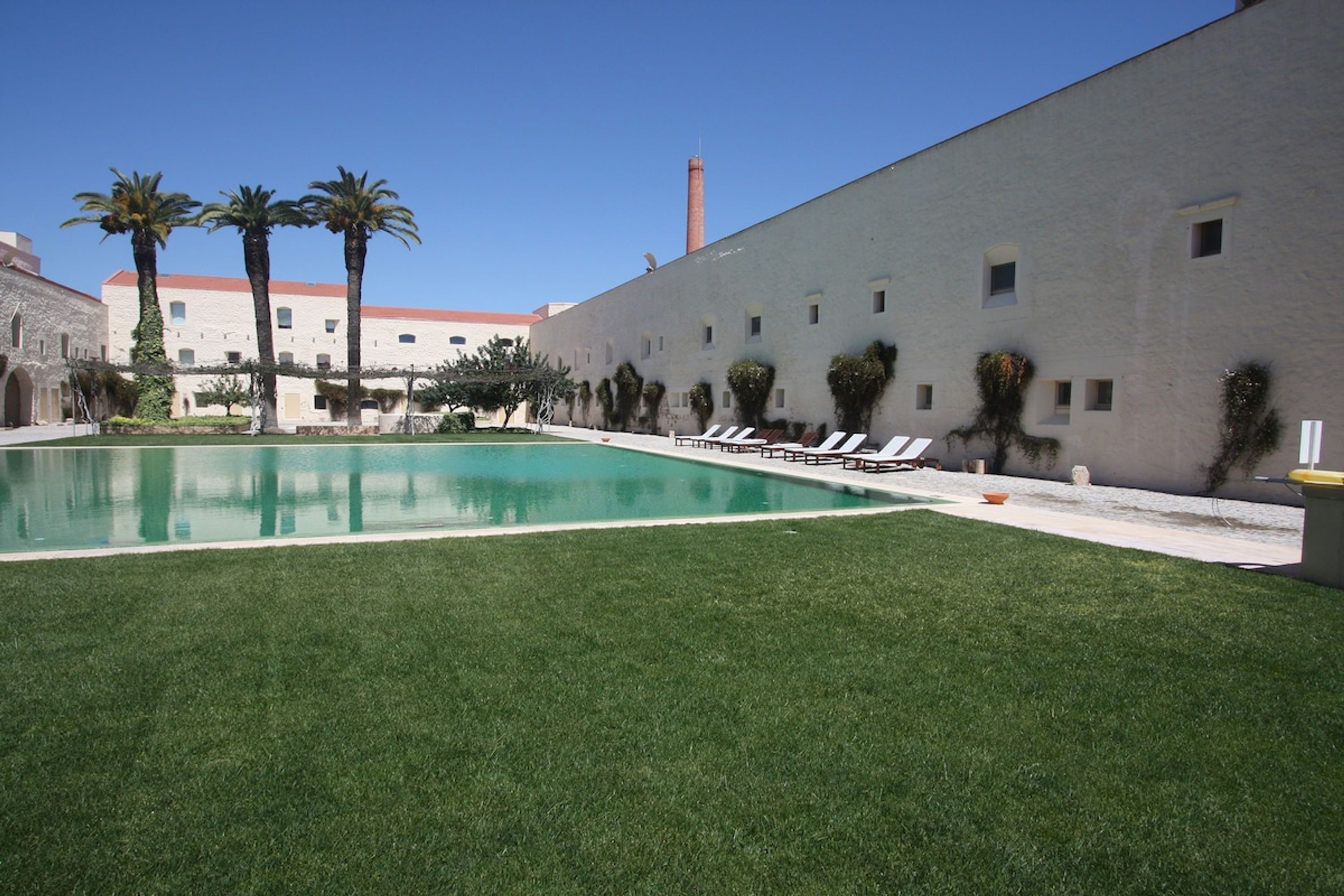 Una piscina con sillones de descanso, palmeras y un edificio con techo de tejas rojas.