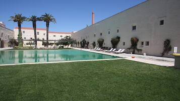 Una piscina con sillones de descanso, palmeras y un edificio con techo de tejas rojas.