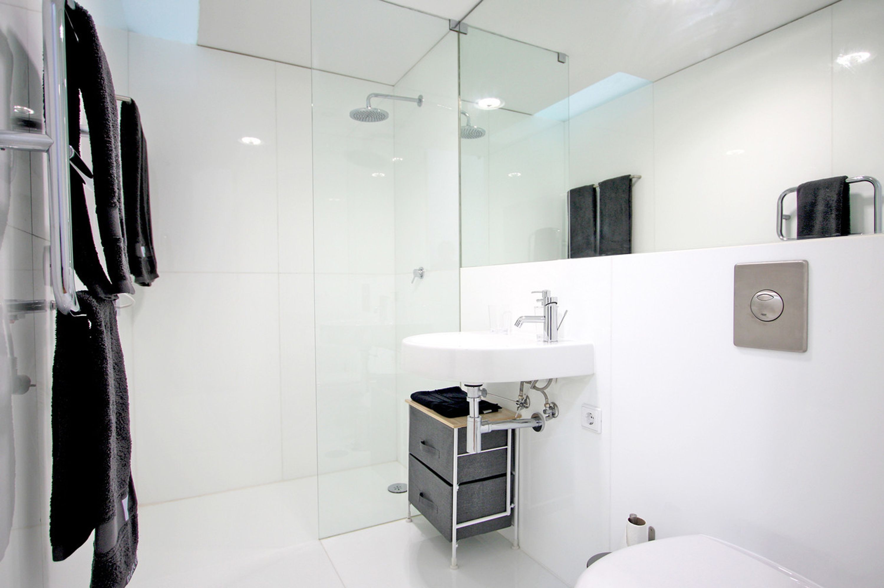 Un bany modern amb plat de dutxa de vidre, un lavabo blanc i un mirall.