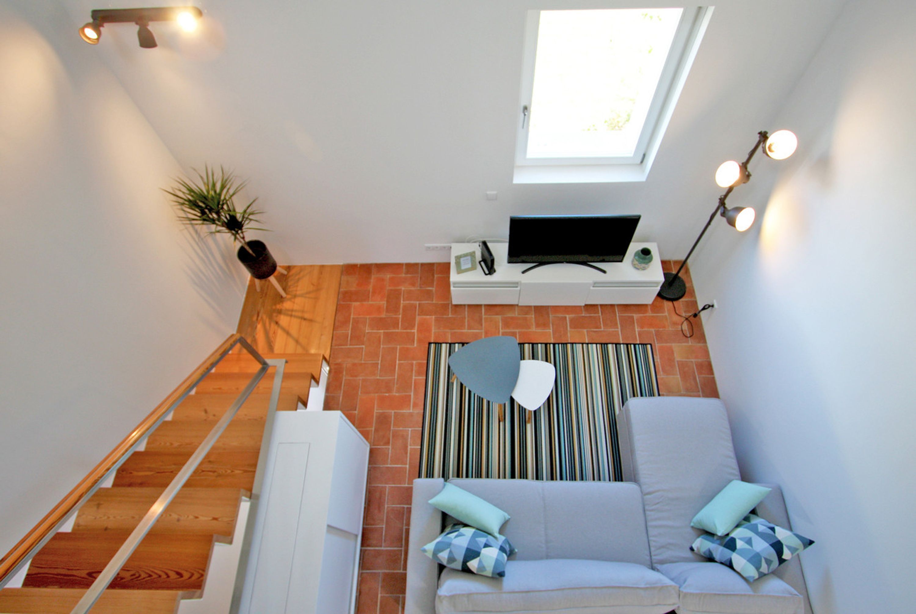 A modern living room with a sofa, a TV, a plant, and a staircase.