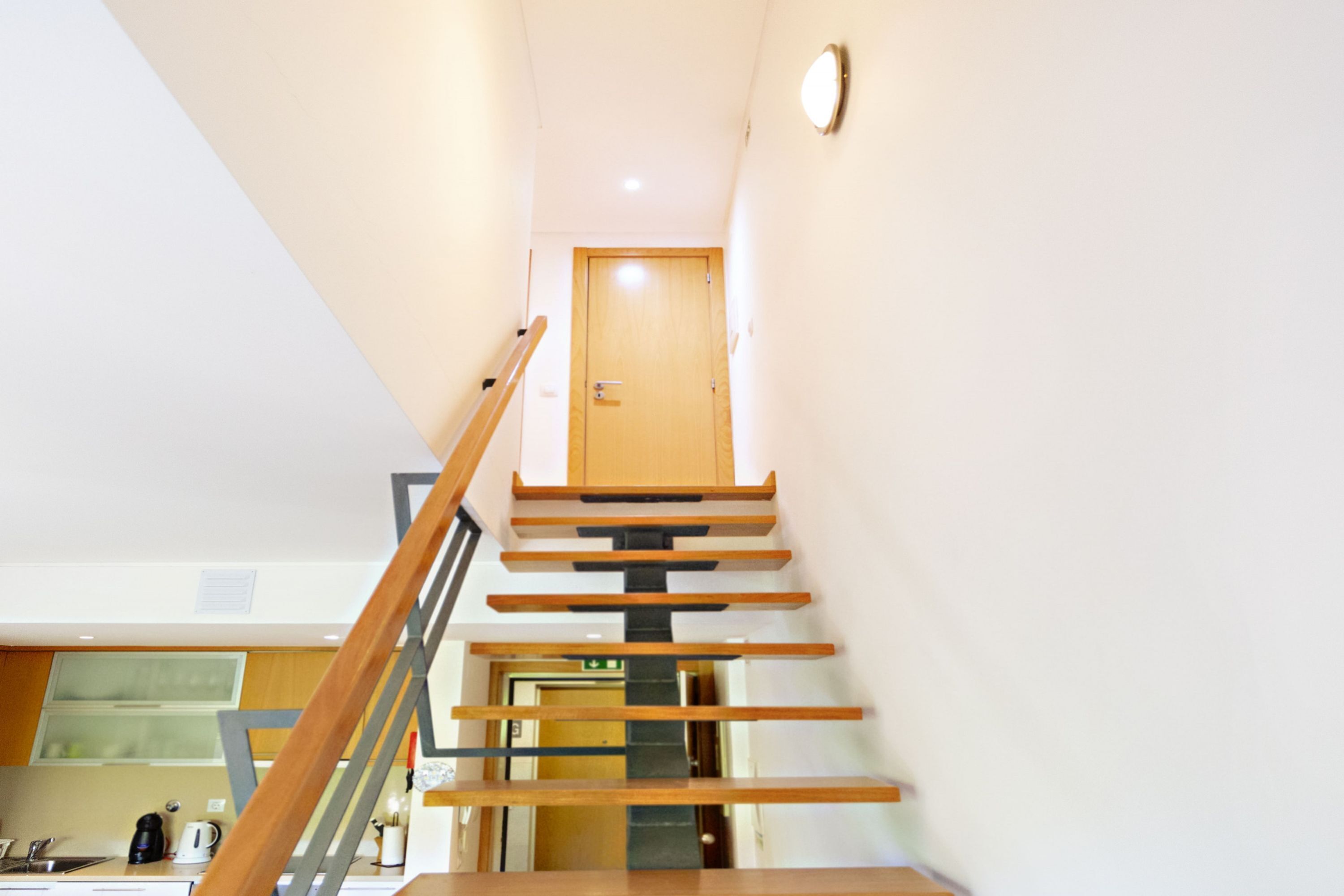 A modern interior with a wooden staircase leading to a door.