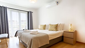 Une chambre d’hôtel moderne dotée d’un grand lit, d’une table de chevet avec une lampe, d’une chaise et offrant une vue sur l’extérieur grâce à une grande fenêtre.