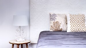 A neatly arranged bedroom with a bed, a round wooden nightstand, a white lamp, and decorative pillows. - S qua - Apt do Rio (Tavira)