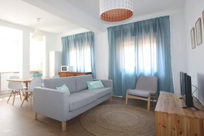 Un salon avec un canapé, un fauteuil, un téléviseur et un bureau en bois.