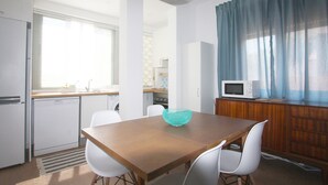 A compact kitchen with a wooden table, white chairs, a microwave, and a window with curtains.