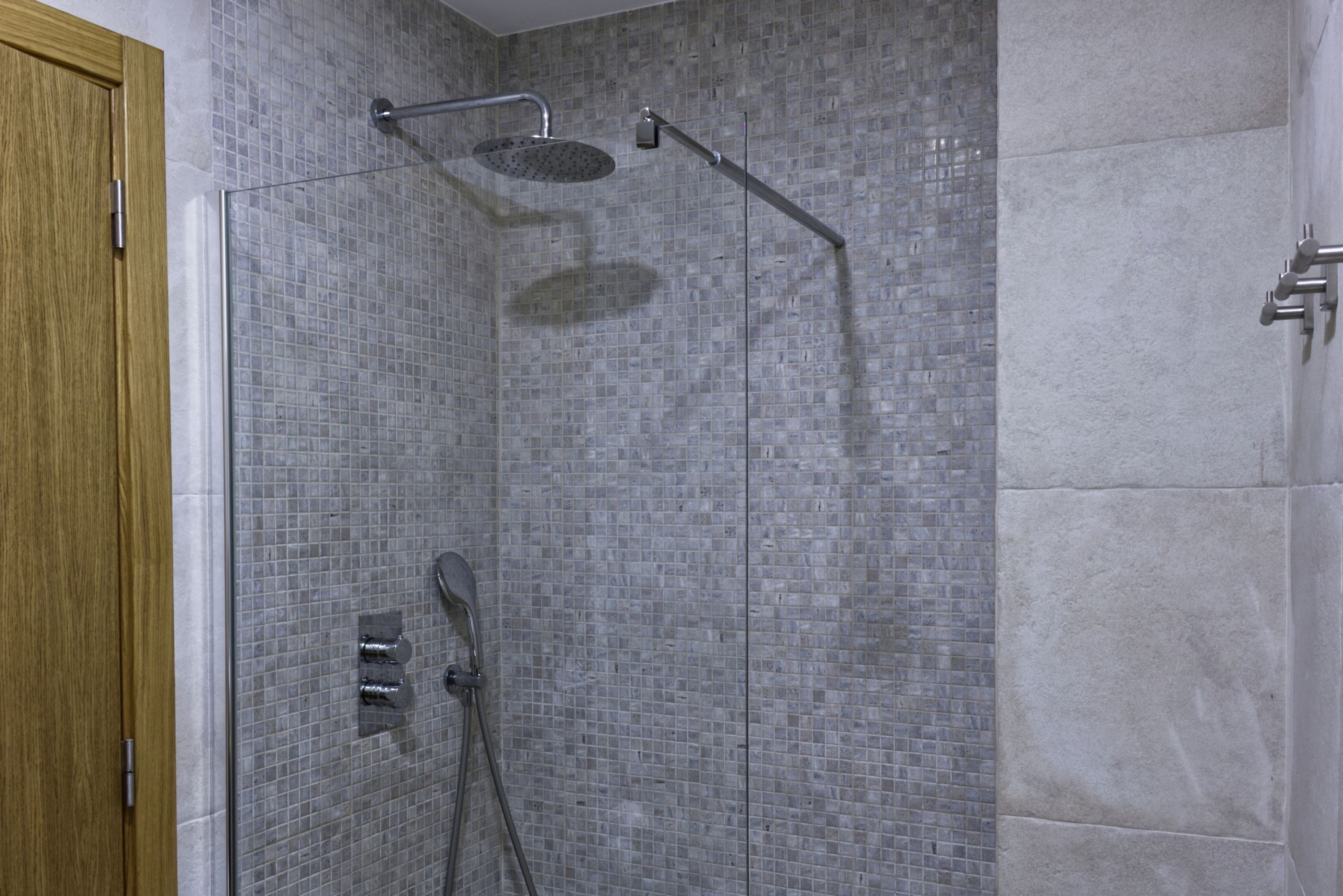 A shower with a glass door, tiled walls, and a wooden door frame.